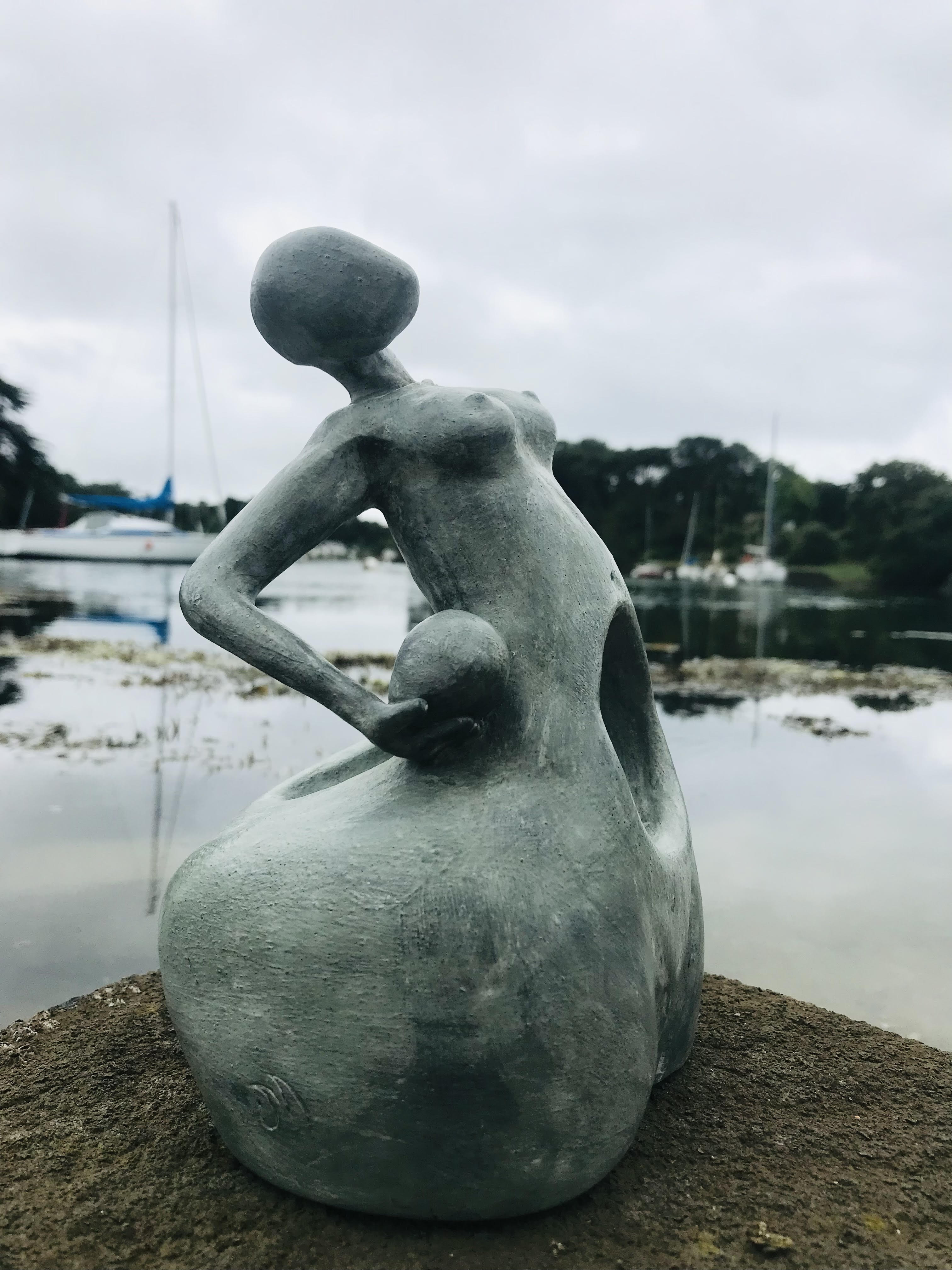 Sculpture en céramique d'une forme féminine sans visage au ventre creux qui soutien une sphere contre son hanche.