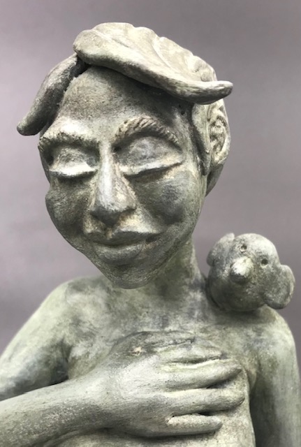 Céramique de femme seins nus avec la main sur le coeur et un oiseau sur l'épaule. Elle a une main sur sa poitrine.