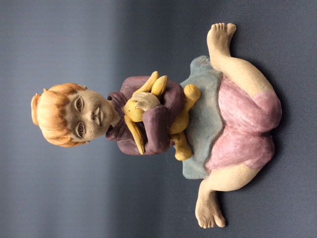 Céramique d'enfant assise par terre, elle embrasse un lapin en pelouche