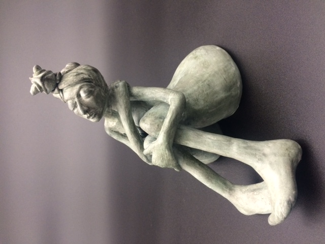 Céramique de femme nue assise, les jambes pliées. Elle a un caméléon sur la tête.