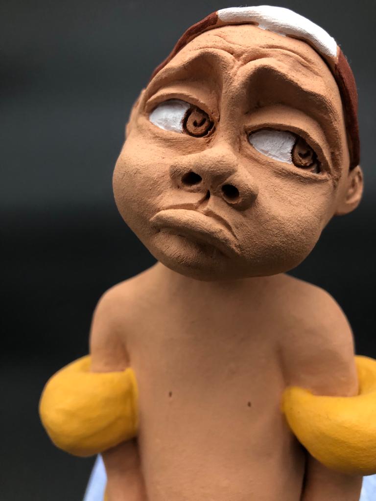 Céramique d'enfant à la tête triste. Il porte une casquette de natation et des brassards.