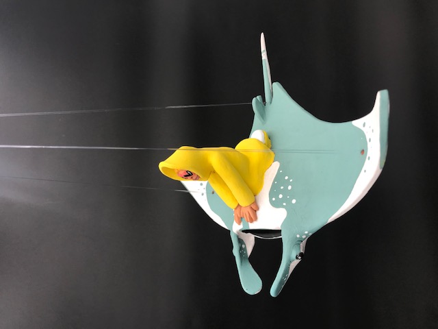 Céramique du personnage en ciré jaune et lunnettes de coeur rouges sur une manta. La pièce a des fils pour l'accrocher au plafond.