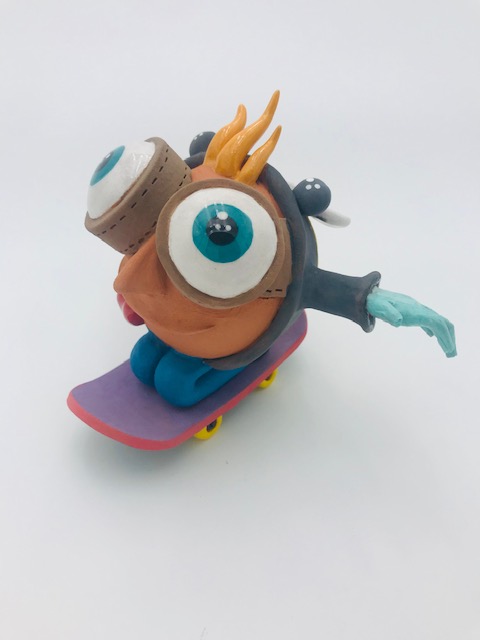 Céramique d'enfant à tête géante à genoux sur skate. Il a des grands yeux et ouvre ses bras. Ses cheveux sont en pointe