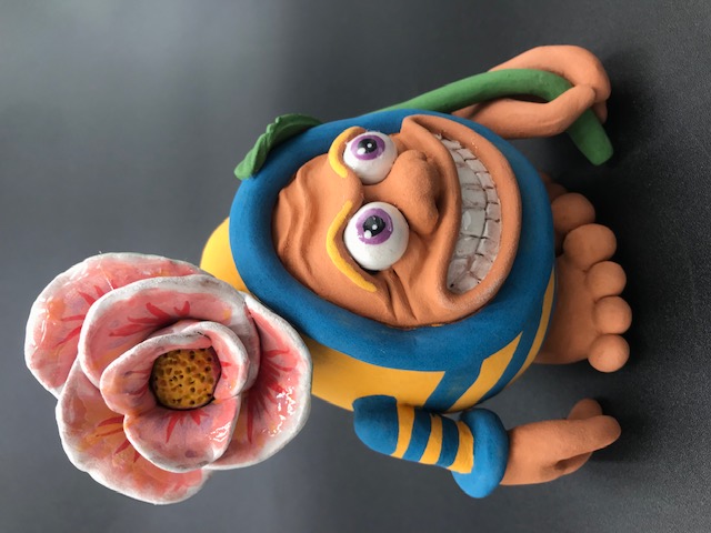 Céramique Tête d'Oeuf. Un personnage qui montre toutes ses dents en riant, il porte une fleur sur sa tête, qui occupe presque tout son corps.