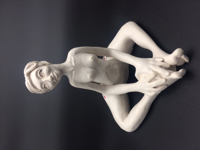 Sculpture en céramique d'une femme aux cheveux courts nue et assise avec les jambes en triangle. Les mains reposent sur les pieds.