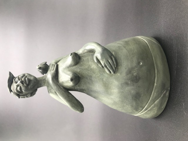 Céramique de femme seins nus avec la main sur le coeur et un oiseau sur l'épaule. Elle a une main sur son ventre et l'autre sur sa poitrine.