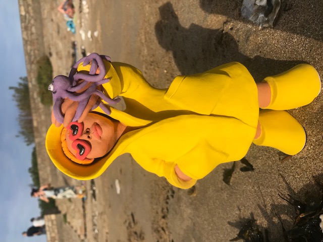 Céramique de personnage en ciré jaune et lunettes rouges à forme de coeur, soutenant un petit poulpe mauve à la main.