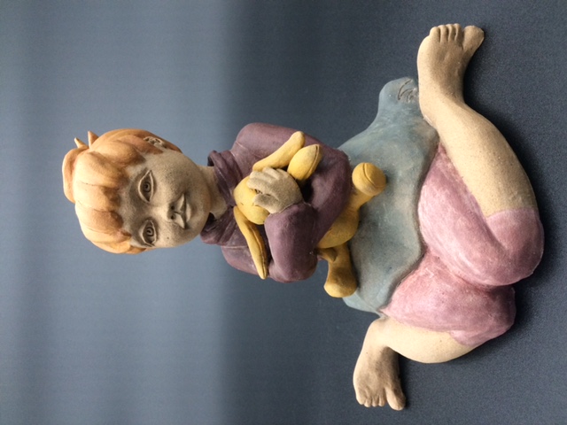 Céramique d'enfant assise par terre, elle embrasse un lapin en pelouche