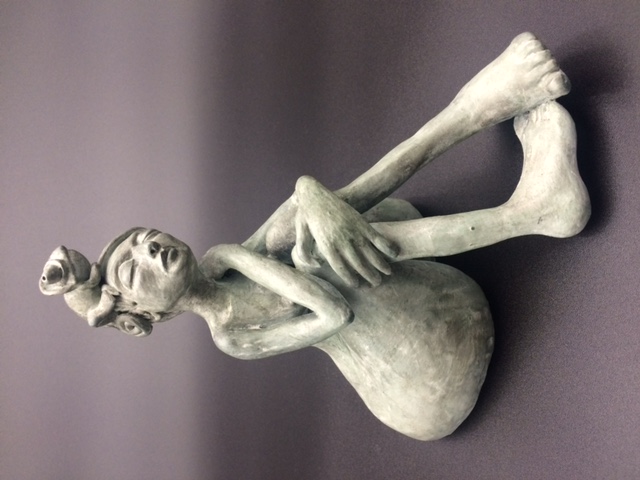 Céramique de femme nue assise, les jambes pliées. Elle a un caméléon sur la tête.