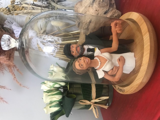 Pièce en céramique qui représente l'image de tête à ceinture d'un couple de mariés, homme et femme. L'homme prend la femme par la taille, ils serrent ses mains. Au fond il y a des fleurs sèches.