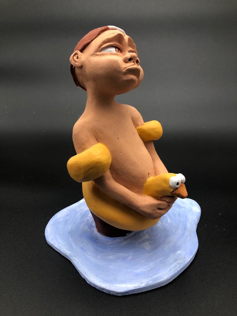 Céramique d'enfant à la tête triste. Il porte une casquette de natation, des brassards et une bouée de canard.