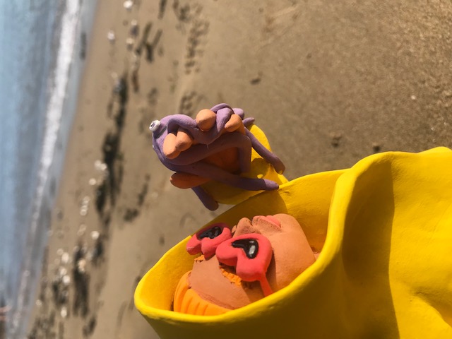 Céramique de personnage en ciré jaune et lunettes rouges à forme de coeur, soutenant un petit poulpe mauve à la main.