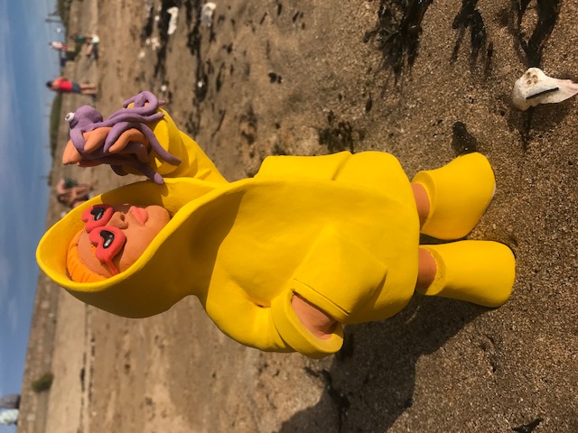 Céramique de personnage en ciré jaune et lunettes rouges à forme de coeur, soutenant un petit poulpe mauve à la main.