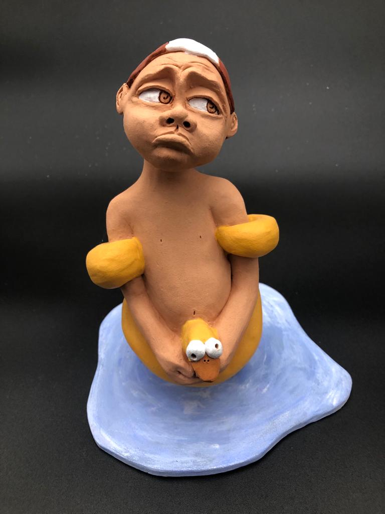 Céramique d'enfant à la tête triste. Il a une casquette de natation, des brassards et une bouée de canard.