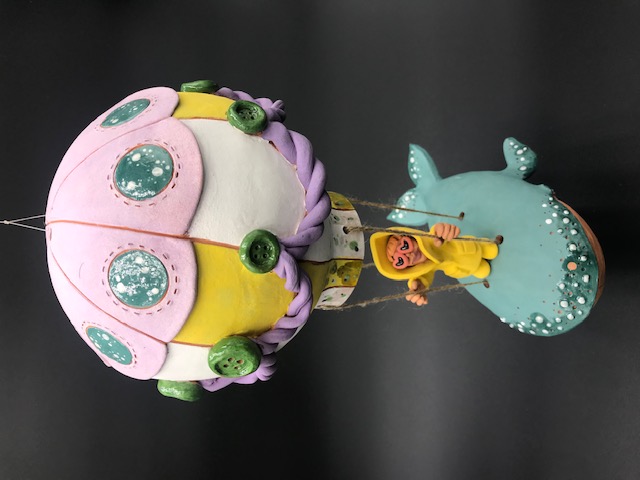 Personnage en ciré jaune montée sur un montgolfière dont la base est un baleine. Vue aérienne