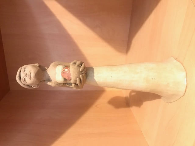 Petite sculpture en céramique d'une femme mince à la robe longue. Elle a une longue queue et regarde vers le haut. El porte dans ses mains un bol avec un minéral