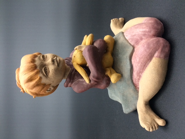 Céramique d'enfant assise par terre, elle embrasse un lapin en pelouche