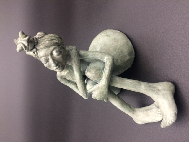 Céramique de femme nue assise, les jambes pliées. Elle a un caméléon sur la tête.