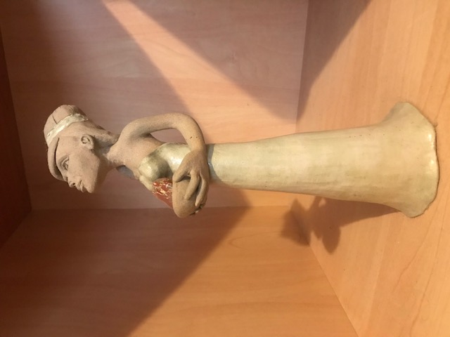 Petite sculpture en céramique d'une femme mince à la robe longue. Elle a une longue queue et regarde vers le haut. El porte dans ses mains un bol avec un minéral