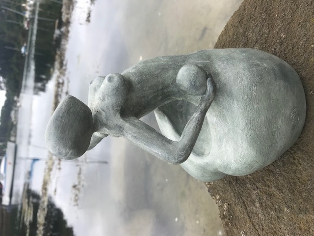 Sculpture en céramique d'une forme féminine sans visage au ventre creux qui soutient une sphère contre son hanche.