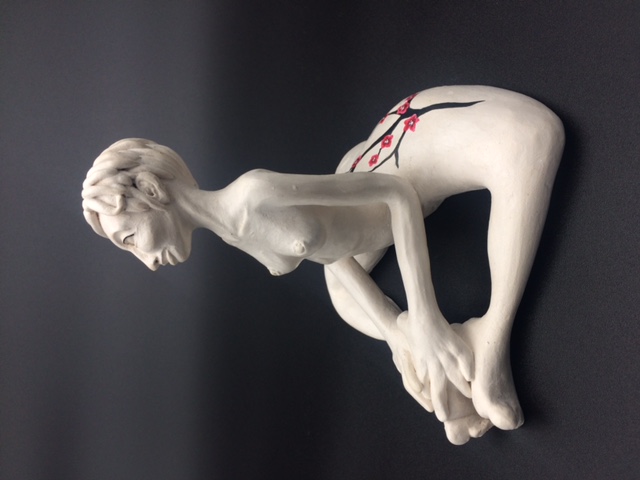 Sculpture en céramique d'une femme aux cheveux courts nue et assise avec les jambes en triangle. Les mains reposent sur les pieds.