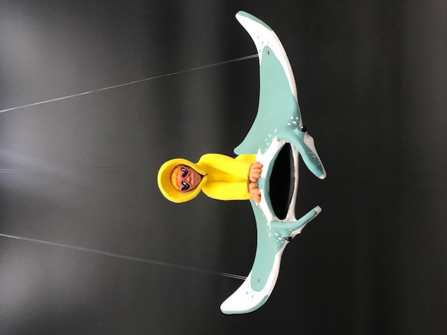 Céramique du personnage en ciré jaune et lunnettes de coeur rouges sur une manta. La pièce a des fils pour l'accrocher au plafond.