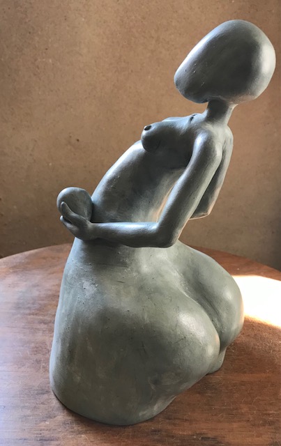 Vue de l'arrière de trois quarts de la sculpture de femme en céramique qui soutient deux grands œufs