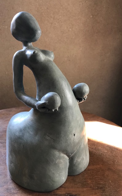 Vue du devant de trois quarts de la sculpture de femme en céramique qui soutient deux grands œufs