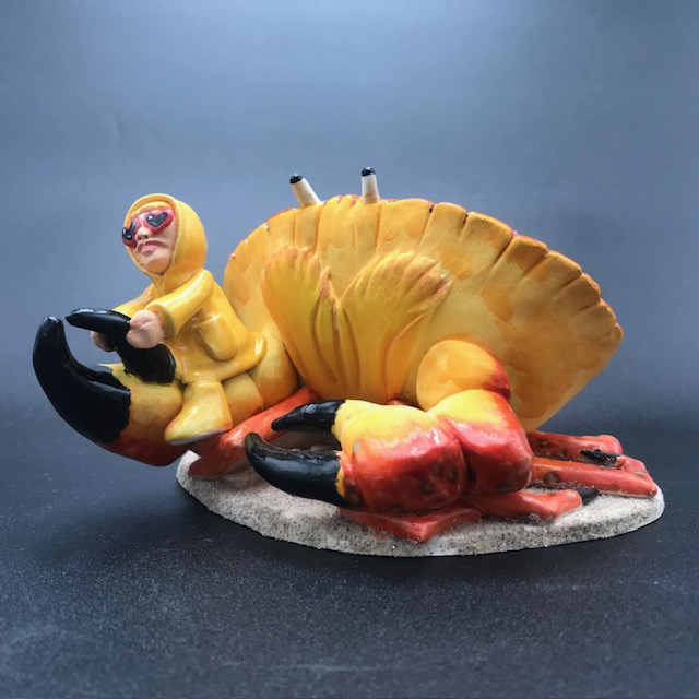 Sculpture en céramique d'une petite fille en ciré jaune à califourchon sur la pince d'un crabe