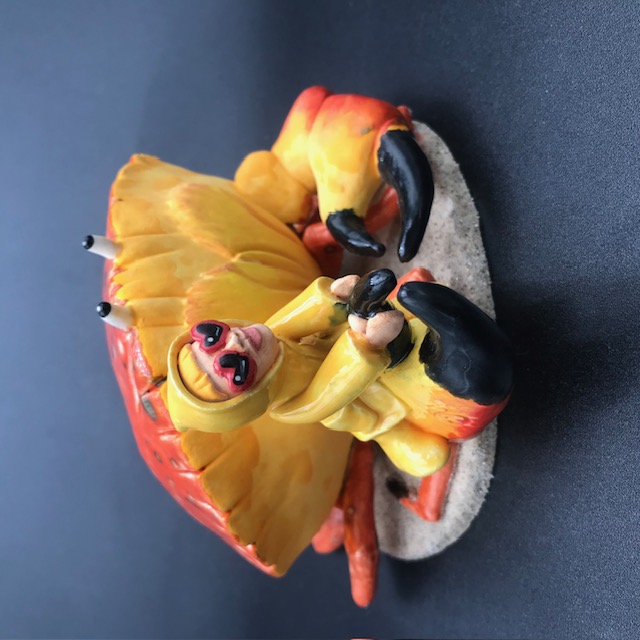 Sculpture en céramique d'une petite fille en ciré jaune à califourchon sur la pince d'un crabe