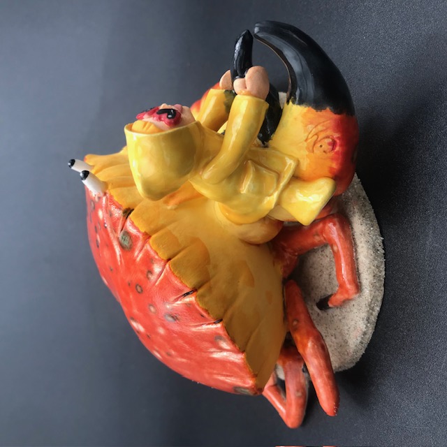 Sculpture en céramique d'une petite fille en ciré jaune à califourchon sur la pince d'un crabe