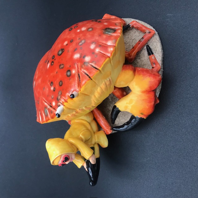 Sculpture en céramique d'une petite fille en ciré jaune à califourchon sur la pince d'un crabe