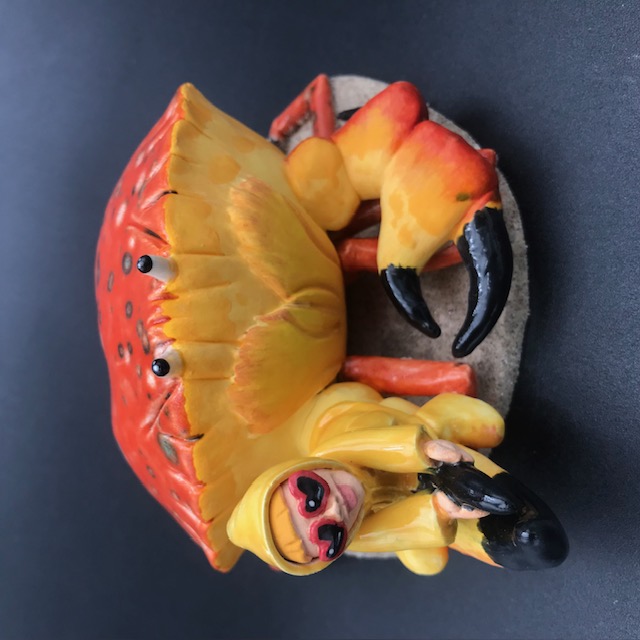 Sculpture en céramique d'une petite fille en ciré jaune à califourchon sur la pince d'un crabe