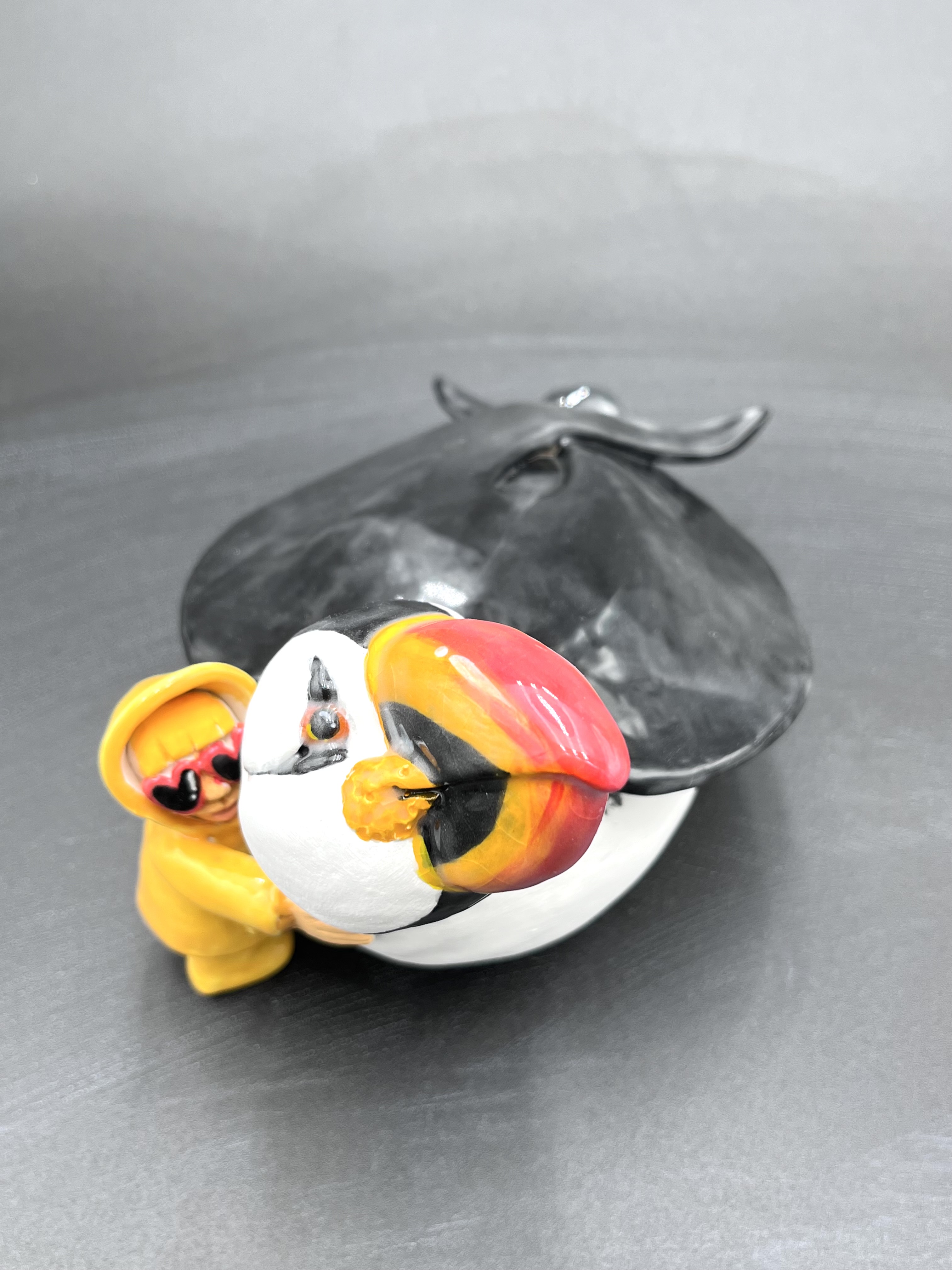 Sculpture en céramique d'un petit personnage en ciré faisant un calin à un macareux