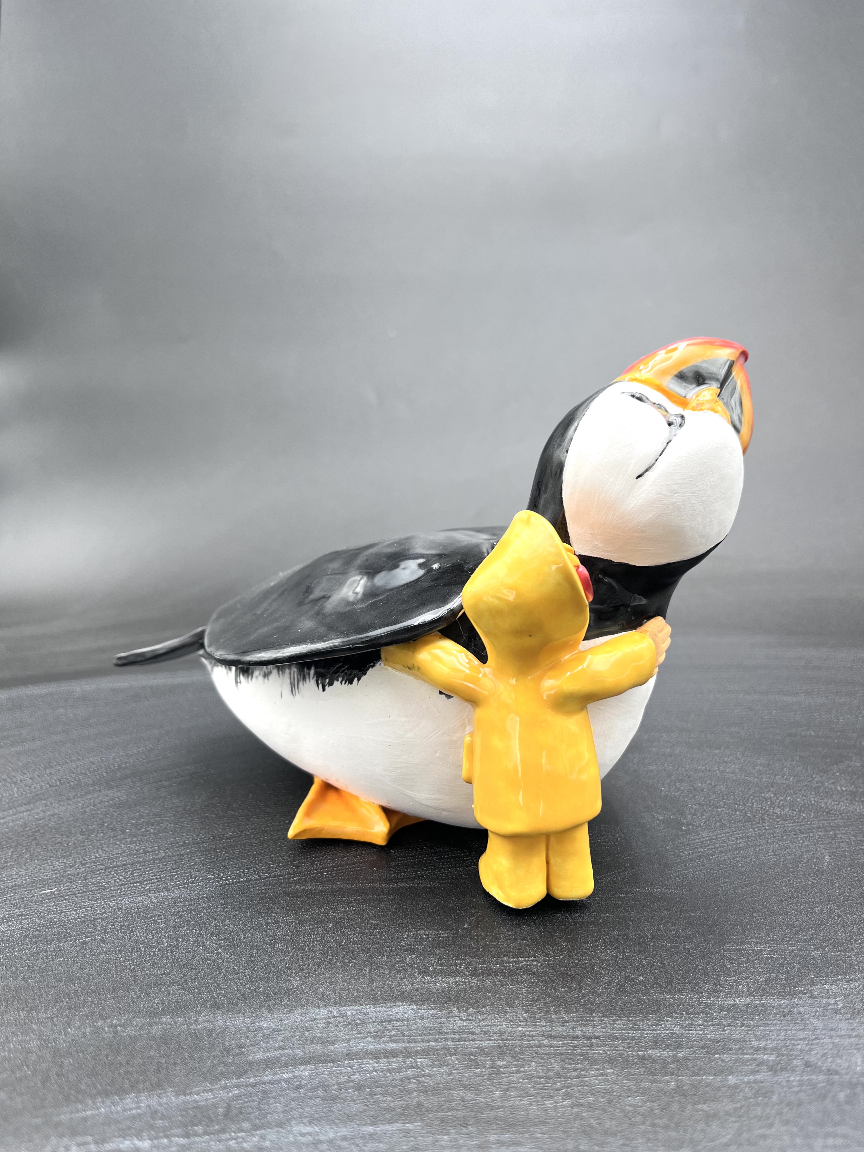 Sculpture en céramique d'un petit personnage en ciré faisant un calin à un macareux