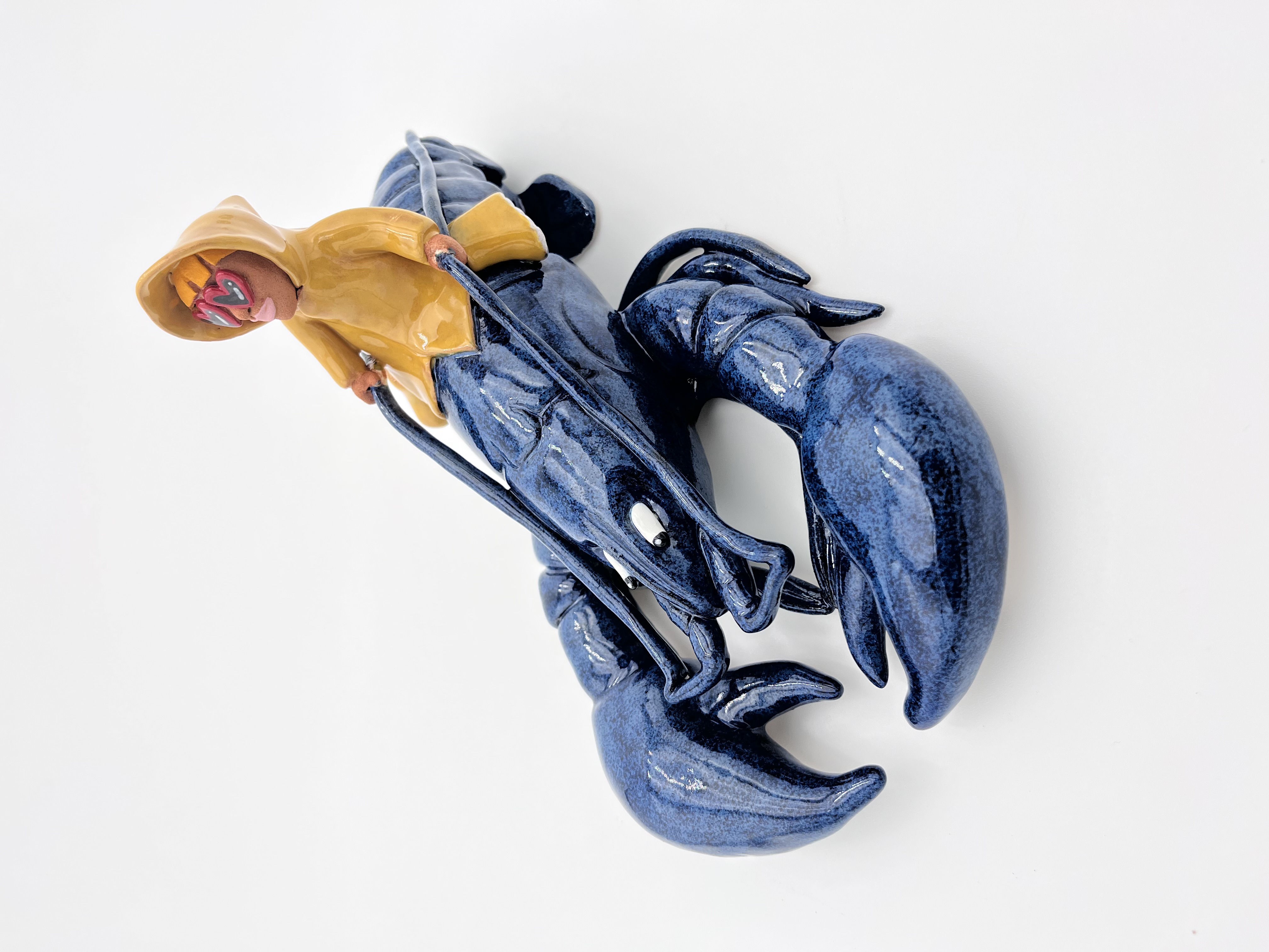 Sculpture en céramique d'un petit personnage en ciré jaune chevauchant un homard bleu