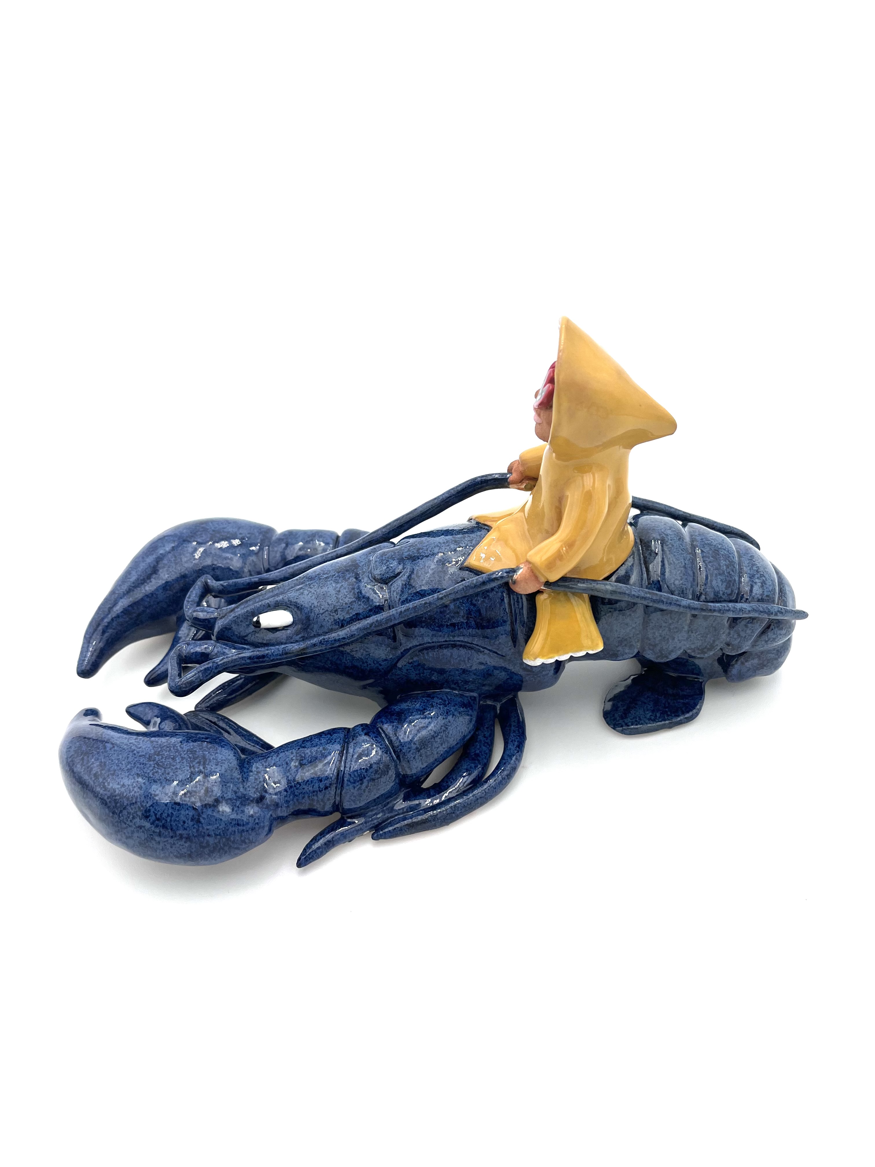 Sculpture en céramique d'un petit personnage en ciré jaune chevauchant un homard bleu