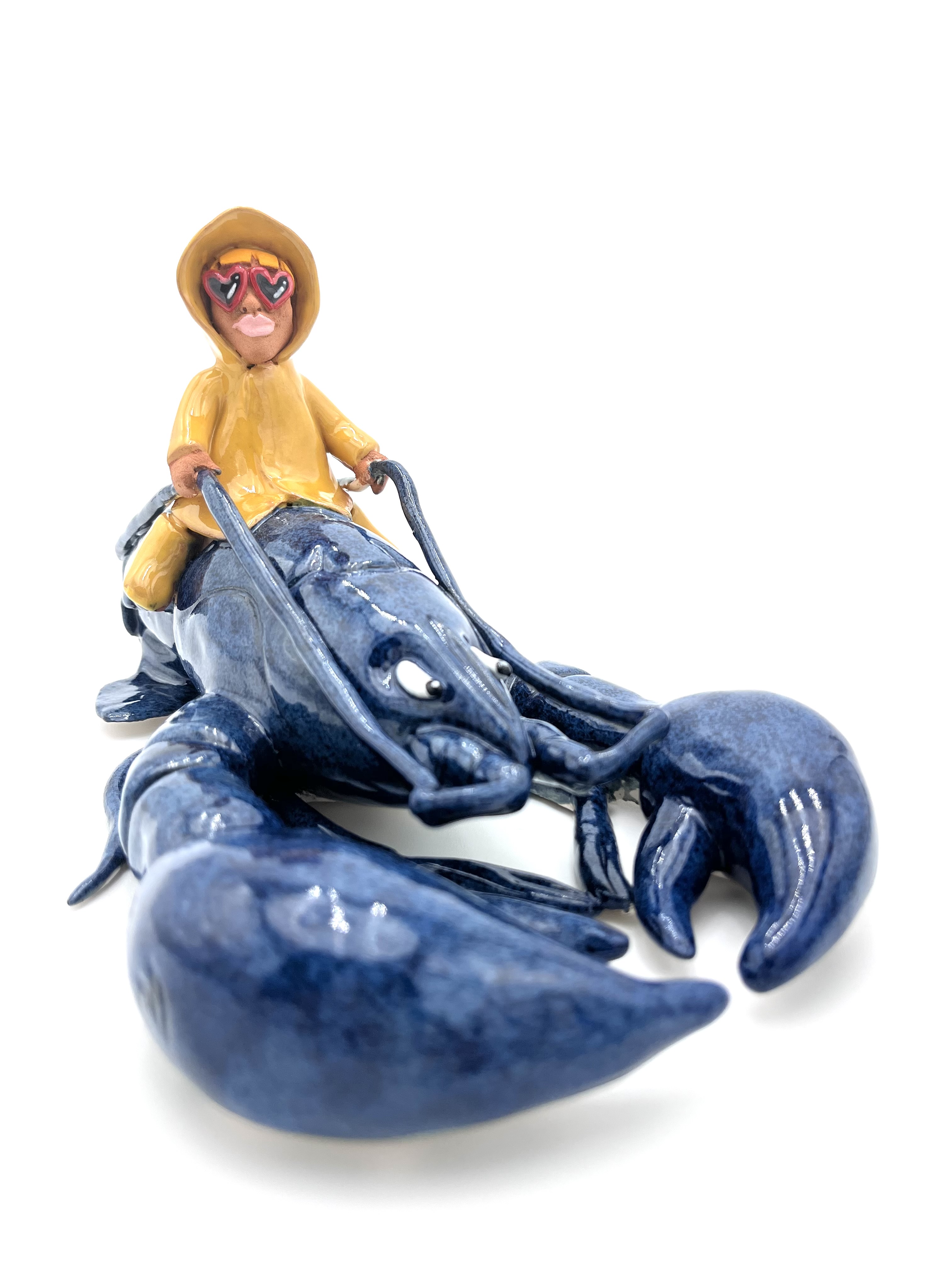 Sculpture en céramique d'un petit personnage en ciré jaune chevauchant un homard bleu