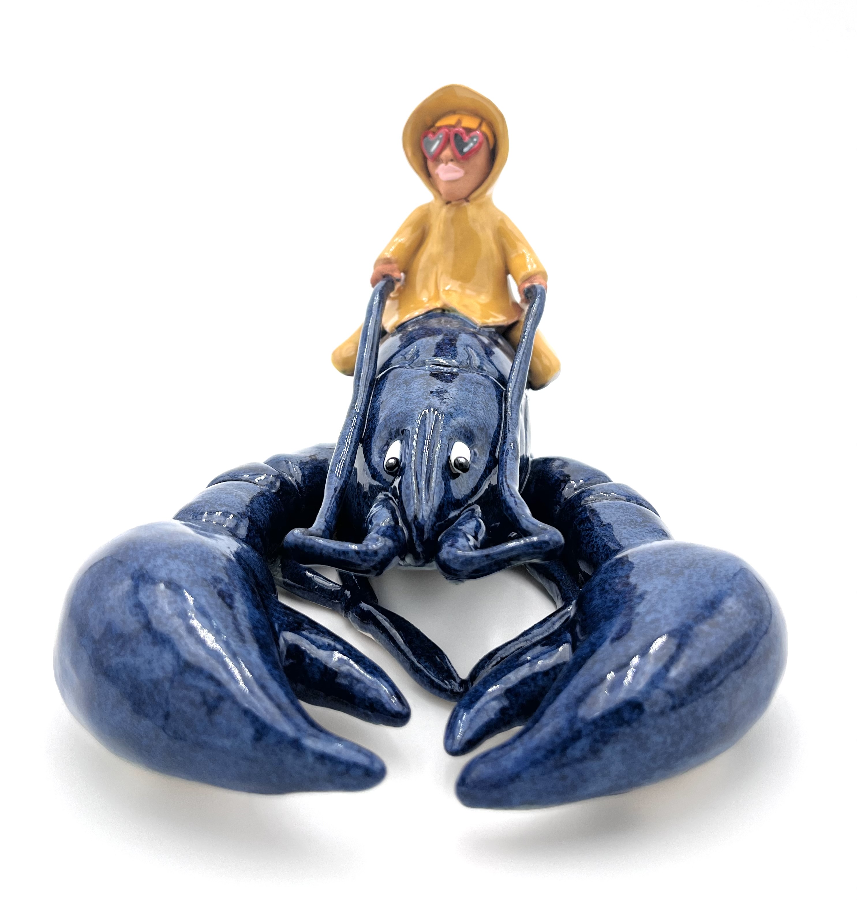 Sculpture en céramique d'un petit personnage en ciré jaune chevauchant un homard bleu